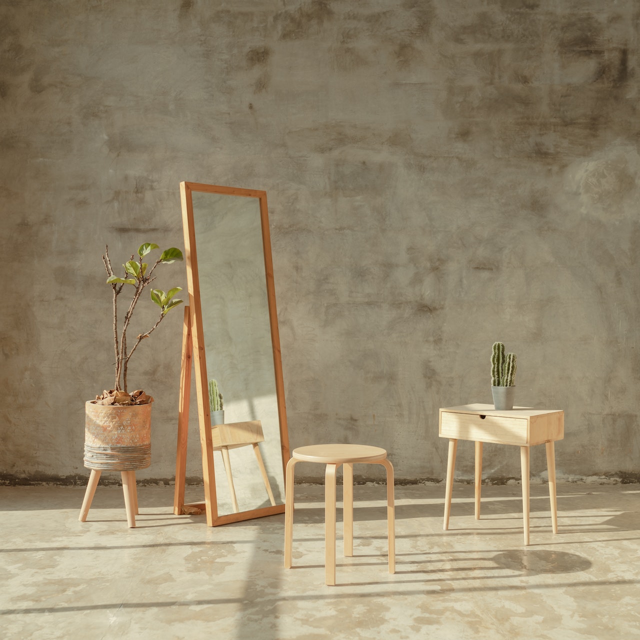 A chair, bedside table, mirror and plant in an empty room with warm light shining in